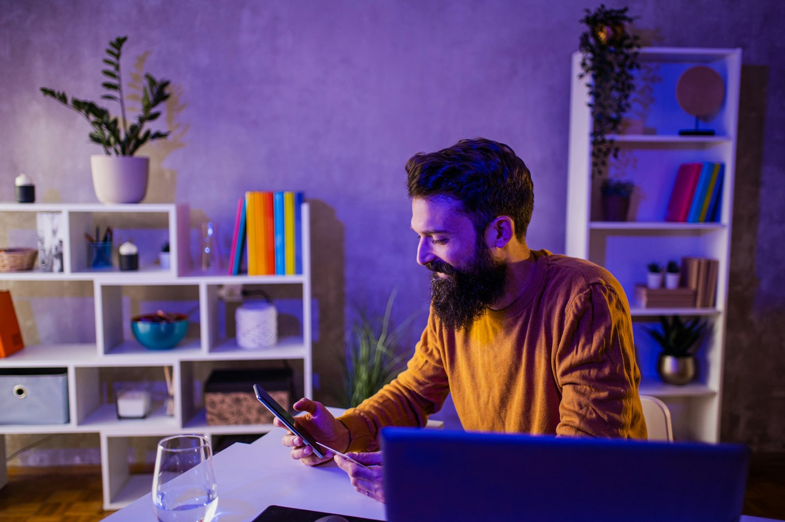 A happy hipster is sitting at a neon-lighted home office and shopping online in a web shop.